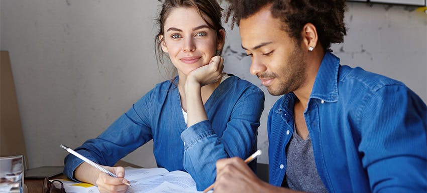 Two interns working together at a desk, taking notes during a remote internship study session.