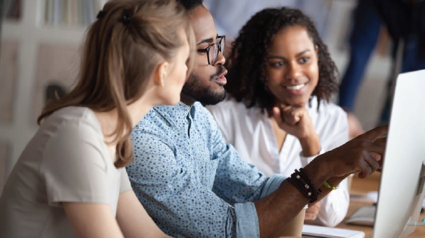 Image of three students who are gathered around a computer and collaborating on a project together