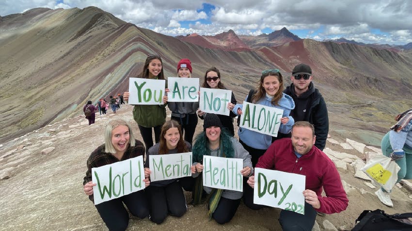 Psychology interns in Peru, pictured on top of Rainbow Mountain, holding signs with the text, You are not alone World Mental Health Day, Intern Abroad HQ
