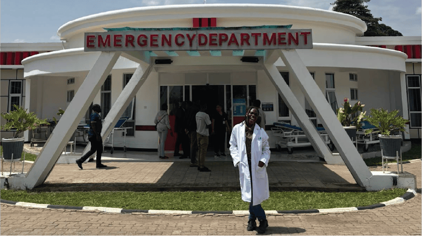 Glodie, an intern in Arusha, Tanzania, smiles and stands outside the Emergency Department building of a hospital