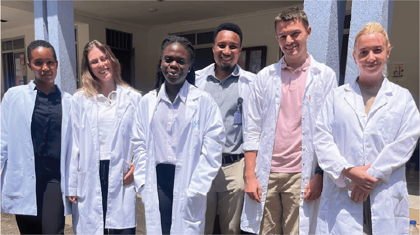 Glodie, an intern in Arusha, Tanzania, is pictured with a group of medical interns. The students are standing outside a hospital building, wearing white lab coats, and smiling