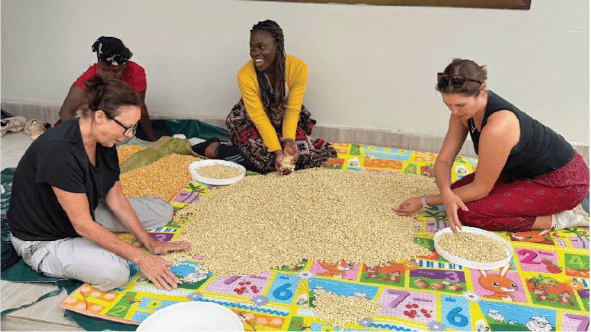 Glodie, an intern in Arusha, Tanzania, smiles and sits with a group of women, who are sorting food together