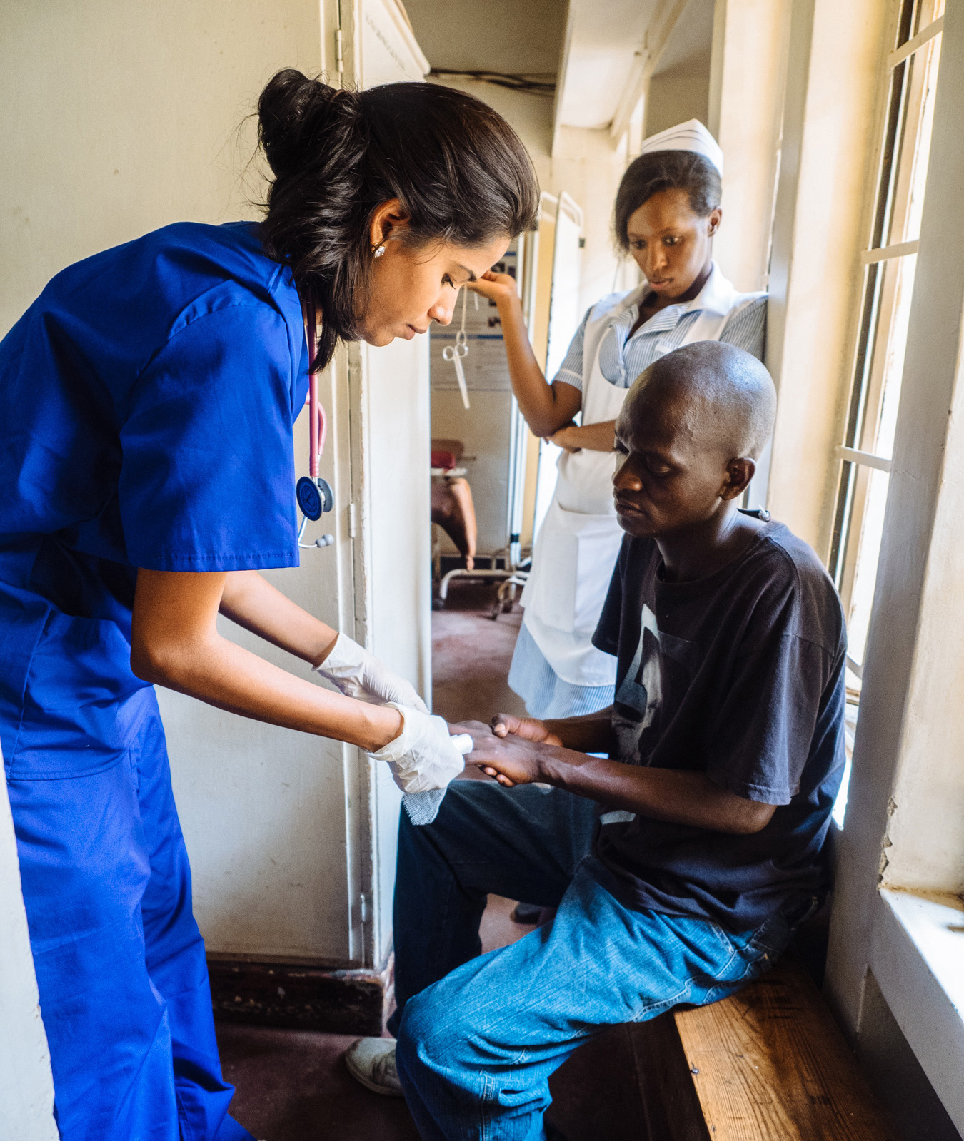Healthcare intern in scrubs treats a patient under supervision at a medical clinic.