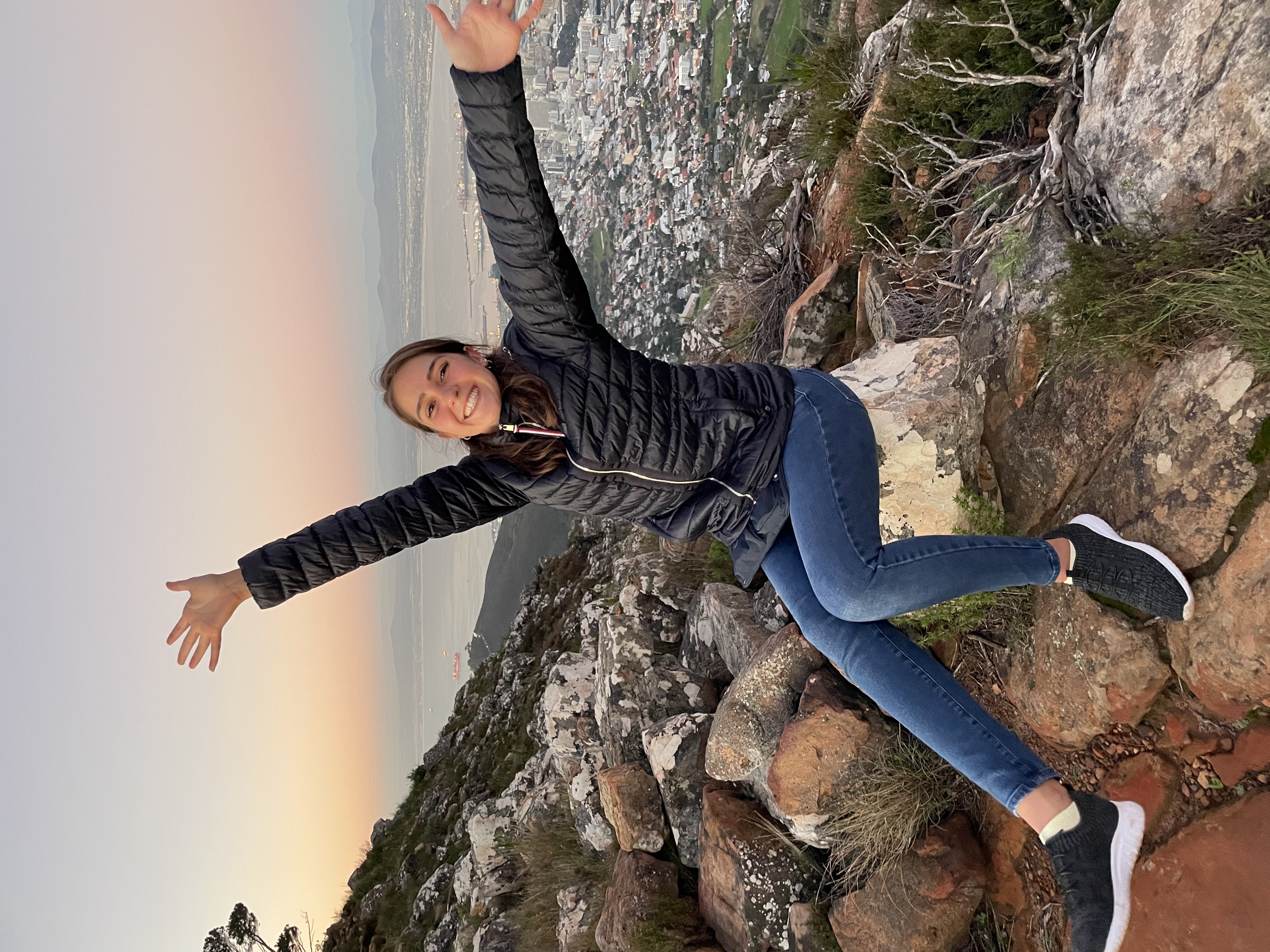 Smiling intern celebrates a scenic hike at sunset overlooking Cape Town from a mountain viewpoint.
